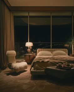 a bedroom with a bed, chair and large window overlooking the city lights at night