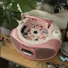 a pink and white radio sitting on top of a table next to a potted plant