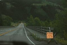 an orange sign sitting on the side of a road in front of a lush green hillside