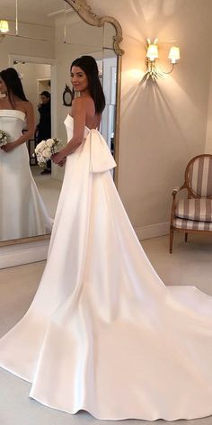 a woman standing in front of a mirror wearing a wedding dress with bow at the back