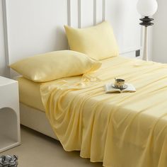 a bed with yellow sheets and pillows in a white room next to a night stand