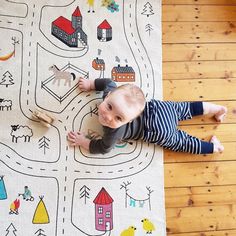 a baby laying on the floor next to a rug with cars and houses drawn on it