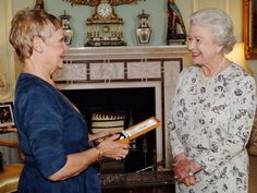 two women standing next to each other in front of a fire place with a clock on the wall