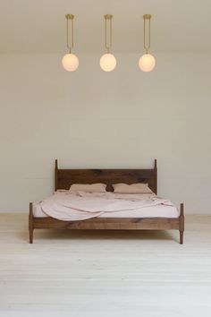 a bed sitting under three lights in a bedroom next to a white wall and wooden floor