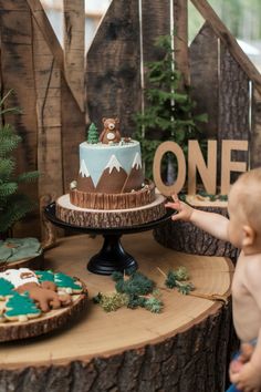 One Happy Camper 1st birthday party setup featuring a Camp First Birthday Cake with a bear topper and mountain design. The rustic One Happy Camper decor includes wooden accents and forest-themed decorations, perfect for a Camping Themed 1st Birthday Party. The setup also features a variety of One Happy Camper desserts, ideal for an outdoorsy first birthday celebration. Birthday Creative Ideas, Happy Camper 1st Birthday, Camping Theme Cakes, One Happy Camper First Birthday, Explorer Birthday Party, Camping Cakes