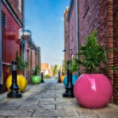 an alley way with colorful balls and plants on either side of the street, surrounded by brick buildings