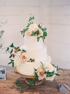 a white wedding cake with flowers and greenery on the top is sitting on a wooden table