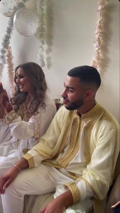 a man and woman sitting next to each other in front of a wall with garlands