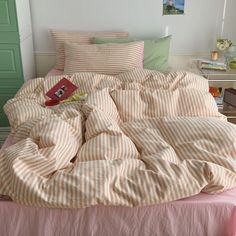 an unmade bed with pink and white striped comforter, pillows and books on it