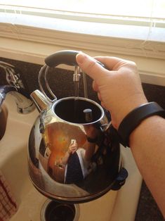 a person holding a tea pot over a stove top burner next to a window