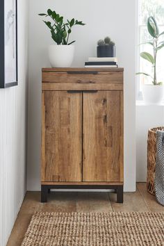 a wooden cabinet sitting on top of a floor next to a plant in a pot