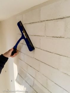 a person using a paint roller on a white brick wall with a blue spatula