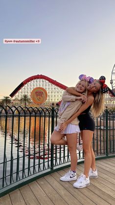 two women hugging each other in front of a roller coaster