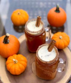 two mugs filled with liquid sitting on top of a wooden tray next to pumpkins