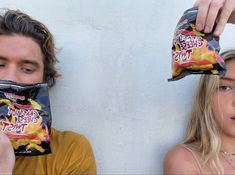 a man holding a bag of cheetos next to a woman with her hair pulled back