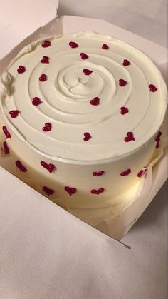 a cake with white frosting and red hearts on it sitting in a cardboard box