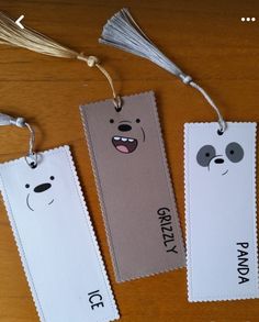 three bookmarks with faces and tassels hanging from strings on a wooden table