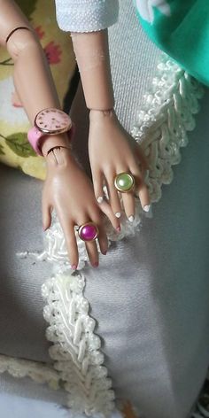 a close up of a doll's hand with rings on it and a pillow