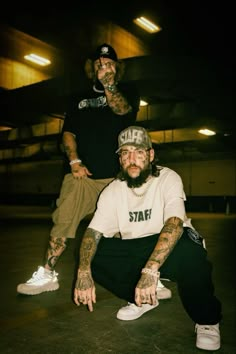 two men with tattoos sitting on the ground