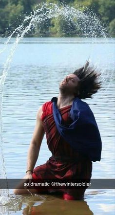 a woman sitting in the water with her hair flying up into the air and splashing on her face