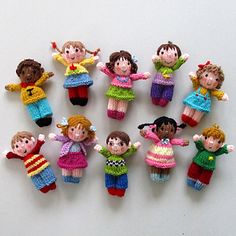 a group of knitted dolls sitting next to each other on a white surface with their hands in the air