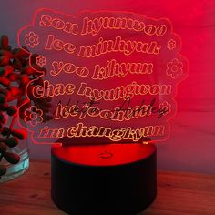 an illuminated sign with the words i love you in different languages on it, sitting next to a vase filled with flowers