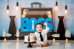 a baby sitting on the floor with a cake in front of him and holding his fist up