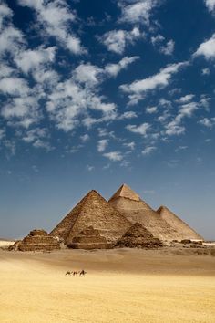 three pyramids in the desert under a cloudy sky