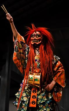 a man with long red hair and makeup holding a stick in his hand while standing next to a building