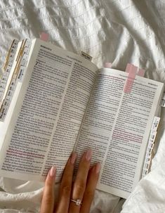 a person laying in bed reading a book with pink stickers on it's pages