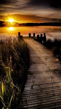 a wooden walkway leading to the water at sunset