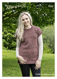 a woman standing in the grass wearing a sweater