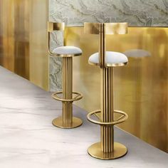 two golden barstools in front of a gold wall and white marble countertop