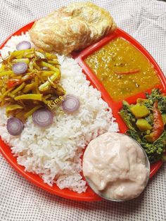 a red plate topped with rice and veggies covered in sauce next to bread