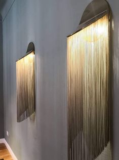 two lights that are on the side of a wall in front of a mirror with fringes hanging from it