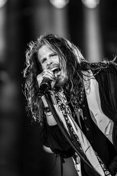 a man with long hair holding a microphone in his hand and singing into the microphone