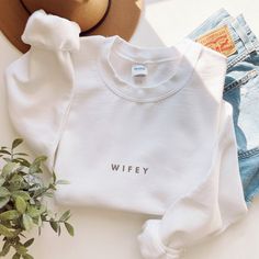 a white sweatshirt with the word wife on it next to some denim shorts and a hat