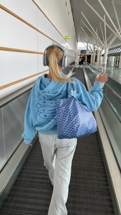 a woman walking down an escalator carrying a blue bag and wearing headphones