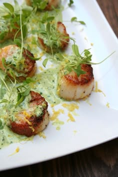 some scallops are on a white plate with green sauce and garnish