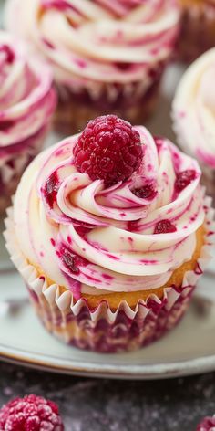 cupcakes with white frosting and raspberry toppings on a plate