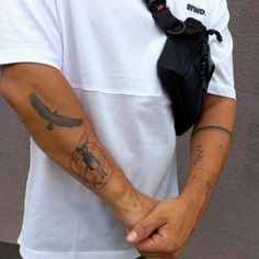 a man with a tattoo on his arm holding onto a camera bag while standing next to a wall