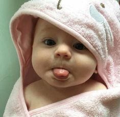 a baby wrapped in a pink towel making a funny face with its tongue sticking out