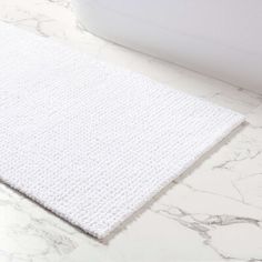 a close up of a white bath mat on a marble floor with a tub in the background