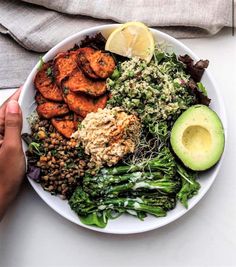 a white plate topped with lots of food next to an avocado and lemon wedge