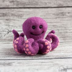 a purple octopus stuffed animal sitting on top of a wooden floor next to a white wall