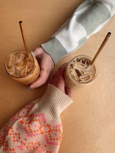 two people holding drinks on top of a wooden table next to each other and one person wearing a sweater