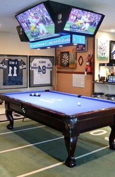 a pool table in a room with two televisions on the wall and other sports memorabilia