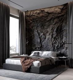 a large bed sitting next to a window with curtains on the sides and a rock wall behind it