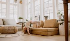 a woman is standing on her head in the middle of a living room with large windows