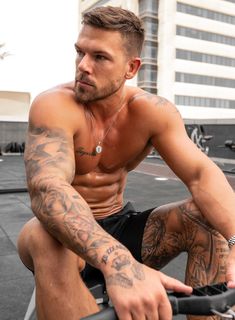 a shirtless man sitting on top of a bike next to a tall building with lots of tattoos